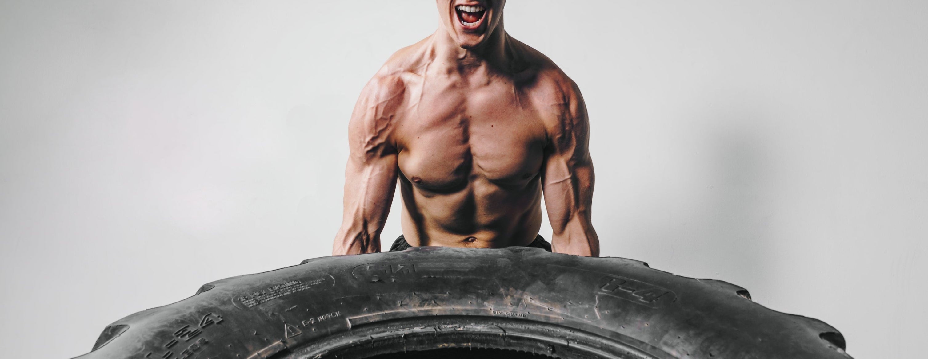 Muscular man lifting a large tire against a gray background
